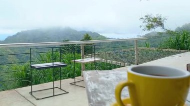 Açık ve puslu manzaranın tadını çıkarırken bir fincan sıcak kahvenin tadını çıkarın. Tumpeng Menoreh, Endonezya 'nın Yogyakarta şehrinde güzel bir turistik yerdir..