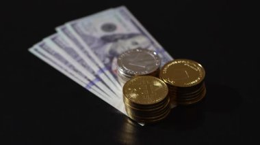 Stacked physical cryptocurrency coins. Bitcoin, Ethereum, and Litecoin, neatly placed on a single US 100 bill over a black background, digital wealth meeting traditional fiat currency.