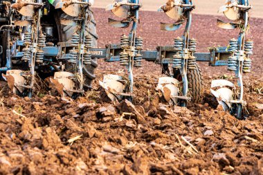 Büyük, modern bir traktör tarlayı sürerek toprağı ağır bir sabanla çevirir. Görüntü, güçlü tarım makinelerini, tarım arazilerini ve kırsal alandaki saha çalışmalarının başlangıcını gösteriyor..
