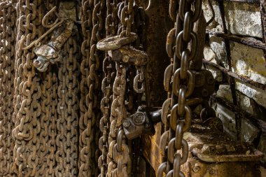 Ağır demir zincirler, kancalar, hava hortumları ve tedarik kabloları aktif bir kömür madeninin karanlık ve engebeli zemininde uzanıyor. Endüstriyel ekipmanlar ve loş yeraltı ortamı zor çalışma koşullarını vurguluyor.