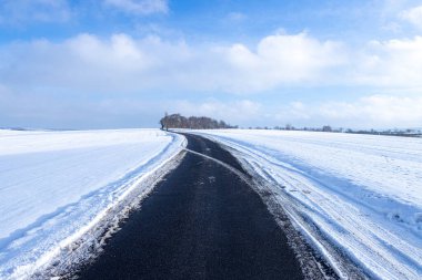 A snow-covered field stretches to the horizon, creating a vast, open space without vegetation or signs of life. The surface appears almost untouched, broken only by a few small footprints in the fresh snow.