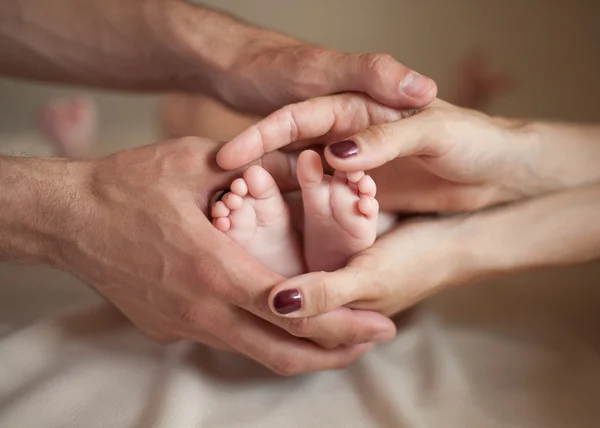 Las manos masculinas y femeninas sostienen los pies del pequeño bebé — Foto de Stock