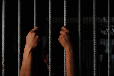 Bir çift erkek eli ve bir alın, bir hapishane hücresinin sert beyaz metal parmaklıklarına bastırılır, yüzü derin gölgelerle gizlenmiş, hapsedilme, suçluluk, ve em temaları taşınır