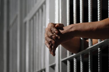  Bir çift erkek eli ve bir alın, bir hapishane hücresinin sert beyaz metal parmaklıklarına bastırılır, yüzü derin gölgelerle gizlenmiş, hapsedilme, suçluluk, ve em temaları taşınır