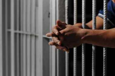  Bir çift erkek eli ve bir alın, bir hapishane hücresinin sert beyaz metal parmaklıklarına bastırılır, yüzü derin gölgelerle gizlenmiş, hapsedilme, suçluluk, ve em temaları taşınır