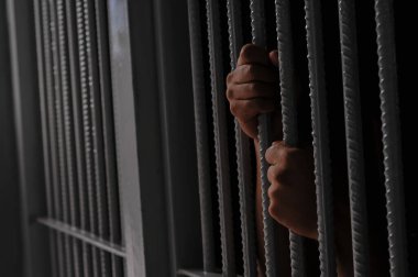 Mahkûmun elleri siyah arka planda parmaklıklar ardında.