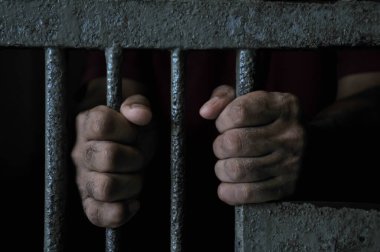 Mahkûmun elleri siyah arka planda parmaklıklar ardında.