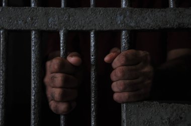 Mahkûmun elleri siyah arka planda parmaklıklar ardında.