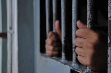 Mahkûmun elleri siyah arka planda parmaklıklar ardında.