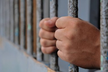 Mahkûmun elleri siyah arka planda parmaklıklar ardında.