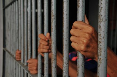 Mahkûmun elleri siyah arka planda parmaklıklar ardında.