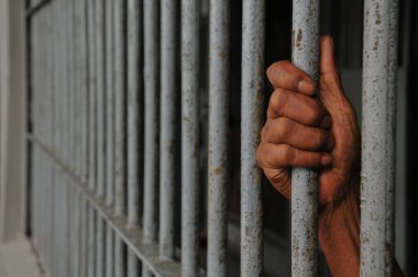 Mahkûmun elleri siyah arka planda parmaklıklar ardında.