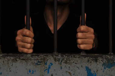 Mahkûmun elleri siyah arka planda parmaklıklar ardında.