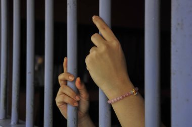 Mahkûmun elleri siyah arka planda parmaklıklar ardında.