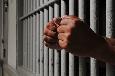 Karanlık bir hücrede parmaklık tutan bir mahkumun yakın çekimi. Hapis, ceza, hapsedilme ve ceza adaleti kavramı.