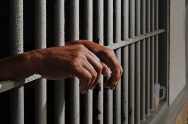 Karanlık bir hücrede parmaklık tutan bir mahkumun yakın çekimi. Hapis, ceza, hapsedilme ve ceza adaleti kavramı.