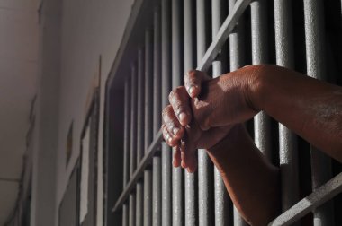 Karanlık bir hücrede parmaklık tutan bir mahkumun yakın çekimi. Hapis, ceza, hapsedilme ve ceza adaleti kavramı.