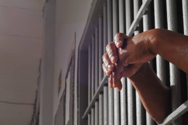 Karanlık bir hücrede parmaklık tutan bir mahkumun yakın çekimi. Hapis, ceza, hapsedilme ve ceza adaleti kavramı.