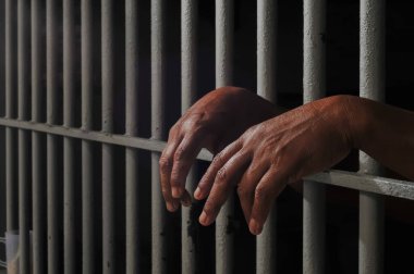 Karanlık bir hücrede parmaklık tutan bir mahkumun yakın çekimi. Hapis, ceza, hapsedilme ve ceza adaleti kavramı.