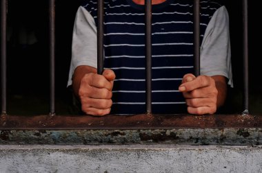 Karanlık bir hücrede parmaklık tutan bir mahkumun yakın çekimi. Hapis, ceza, hapsedilme ve ceza adaleti kavramı.