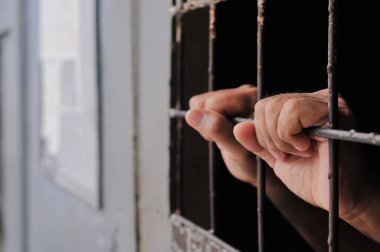 Karanlık bir hücrede parmaklık tutan bir mahkumun yakın çekimi. Hapis, ceza, hapsedilme ve ceza adaleti kavramı.