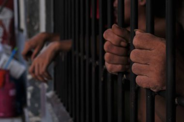 Karanlık bir hücrede parmaklık tutan bir mahkumun yakın çekimi. Hapis, ceza, hapsedilme ve ceza adaleti kavramı.