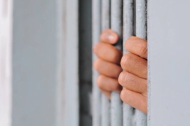 Karanlık bir hücrede parmaklık tutan bir mahkumun yakın çekimi. Hapis, ceza, hapsedilme ve ceza adaleti kavramı.