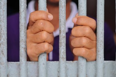 Karanlık bir hücrede parmaklık tutan bir mahkumun yakın çekimi. Hapis, ceza, hapsedilme ve ceza adaleti kavramı.