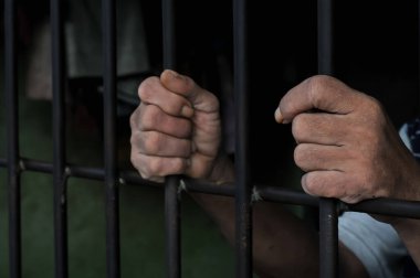 Karanlık bir hücrede parmaklık tutan bir mahkumun yakın çekimi. Hapis, ceza, hapsedilme ve ceza adaleti kavramı.