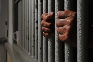 Karanlık bir hücrede parmaklık tutan bir mahkumun yakın çekimi. Hapis, ceza, hapsedilme ve ceza adaleti kavramı.