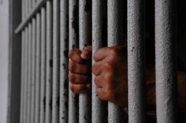 Mahkûmun elleri siyah arka planda parmaklıklar ardında.