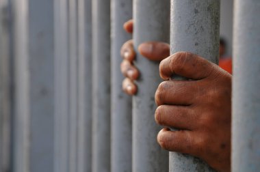 Mahkûmun elleri siyah arka planda parmaklıklar ardında.
