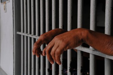 Mahkûmun elleri siyah arka planda parmaklıklar ardında.