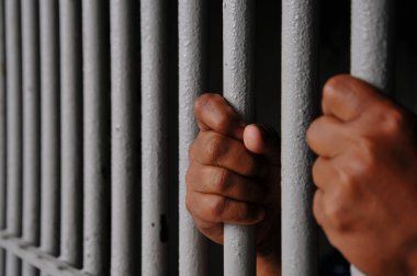 Mahkûmun elleri siyah arka planda parmaklıklar ardında.