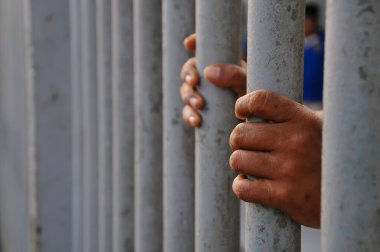 Mahkûmun elleri siyah arka planda parmaklıklar ardında.