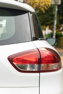 Beyaz bir yolcu vagonunun arka sağ tarafında far, tampon, dikiz aynası ve cam gibi büyük görüntüler var..