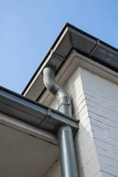 Beyaz tuğla bir binanın köşesindeki metal drenaj borusu.