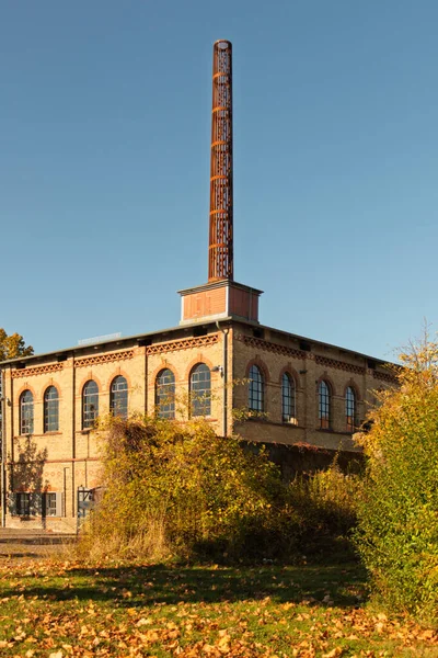 İki katlı eski tuğla bina, büyük pencereler ve Kiel 'deki Howaldtsche Metalgieerei' nin uzun bacası.