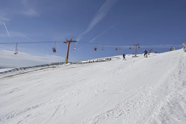 Pista de esquí con cielo azul claro y telesilla con esquiadores —  Fotos de Stock