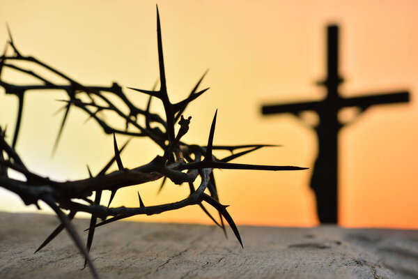Crown of thorns of Jesus Christ against silhouette of catholic cross at sunset background