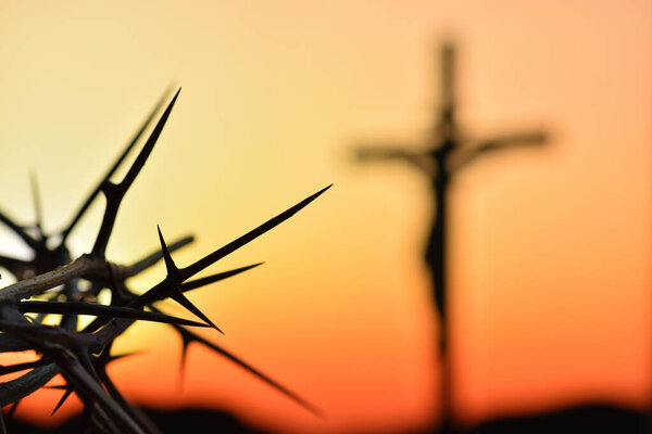 Crown of thorns of Jesus Christ against silhouette of catholic cross at sunset background