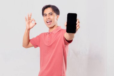 Neşeli genç Asyalı adam boş bir cep telefonu ekranı gösteriyor. Tamam işareti veriyor.