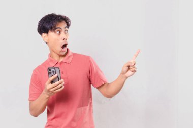 Elinde cep telefonu olan genç bir Asyalı komik bir ifadeyle yan tarafa bakıyor. Ticari kullanım için izole edilmiş.