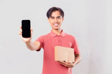 Heyecanlı Asyalı adam boş cep telefonu ekranı gösterirken, karton paket kutusunu dış ticaret kavramı için izole edilmiş olarak tutuyor..