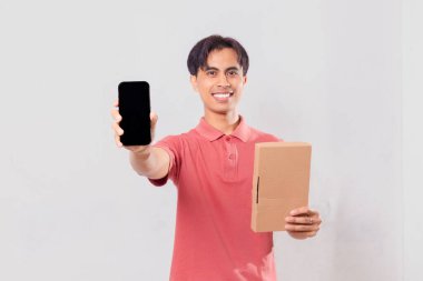 Heyecanlı Asyalı adam boş cep telefonu ekranı gösterirken, karton paket kutusunu dış ticaret kavramı için izole edilmiş olarak tutuyor..