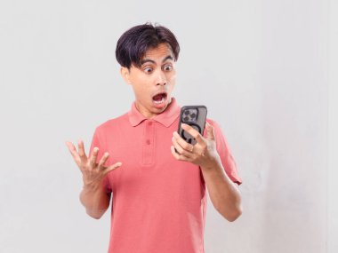 Şok olmuş genç Asyalı adam cep telefonu kullanıyor, arka planda izole edilmiş.