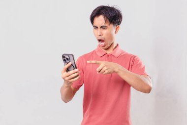 Genç Asyalı adam öfkeyle cep telefonunu kullanıyor, sade arka planda izole edilmiş, ticari ve editörel kullanım için hayal kırıklığı ve duygu gösteriyor.