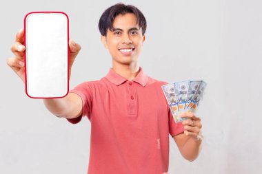 Elinde nakit para tutan ve arka planda boş bir cep telefonu ekranı gösteren neşeli genç bir Asyalı. Reklam ve finansal kavramlar için mükemmel..