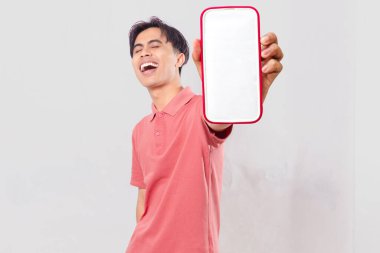 Mutlu, genç, Asyalı, boş akıllı telefon görüntüsü gösteren, gülüşü ve hareketleriyle mobil uygulama promosyonu için sade arka planda izole edilmiş neşeli, genç bir adam..