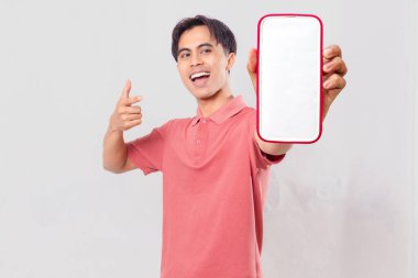 Heyecanlı Asyalı genç adam boş akıllı telefon ekran modelini tutuyor ve mobil uygulama promosyonu için sade arka planda izole ediyor.